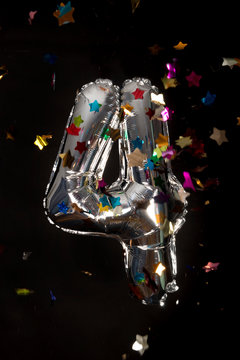 Silver balloon and confetti for  birthday in front of black background