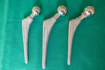 explanted hip prostheses lie spread out on a green surgical drape