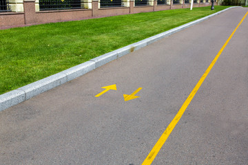 Obraz premium an asphalt road with yellow markings and directional arrows, a roadside with a green lawn and a stone fence.