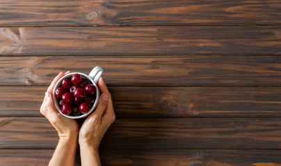 Woman hands with white cup with red cherries on dark wooden desk background. Flat lay. Top view. Backdrop. - Powered by Adobe