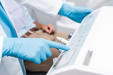 cropped view of dentist in blue latex glove pointing with finger at dental equipment