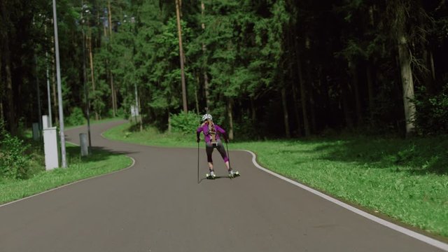TRACKING Caucasian female professional biathlete roller skiing uphill on a forest track during mid-season practice in summer. ARRI Alexa Mini with Cooke S4 prime lenses RAW graded footage