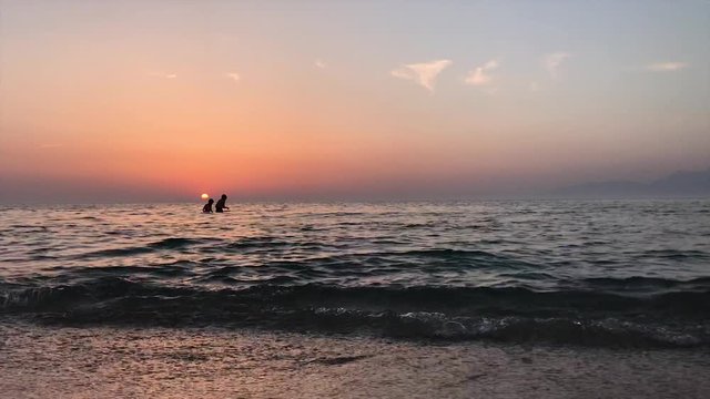 People enjoy a swim in the ocean at sunset  HD Footage