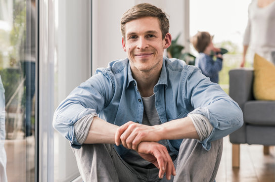 Confident man sitting on floor of his home, smiling