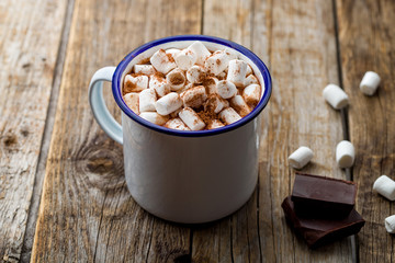 hot chocolate in an iron mug with marshmallow on old wooden background