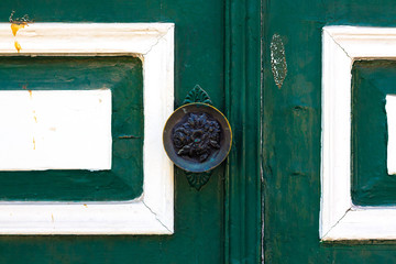 Doorknob on an old green door. The handle is engraved with a pattern in the form of rose flowers.