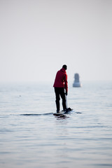 Guy in a red coat on a paddle surfboard in Lake Ontario