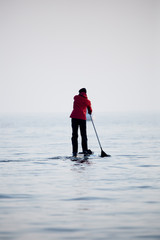 Guy in a red coat on a paddle surfboard in Lake Ontario
