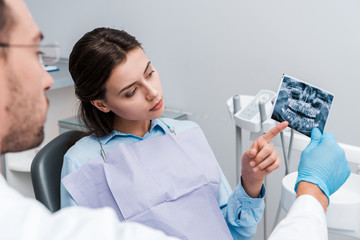 selective focus of woman pointing with finger at x-ray near dentist