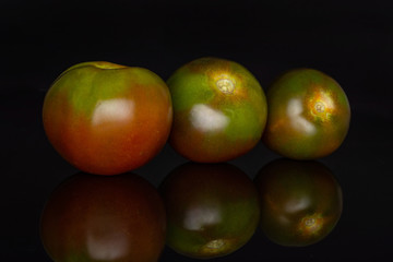 Group of three whole fresh greenish red tomato isolated on black glass