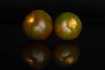 Group of two whole round fresh greenish red tomato isolated on black glass