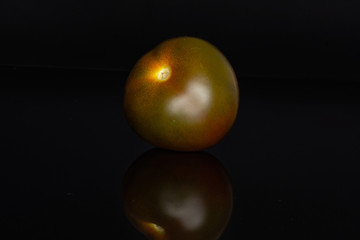 One whole round fresh greenish red tomato isolated on black glass