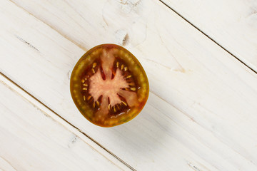 One half of fresh greenish red tomato flatlay on white wood