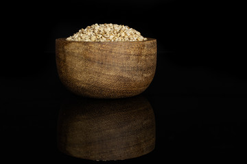 Lot of whole unpeeled sesame seeds in wooden bowl isolated on black glass