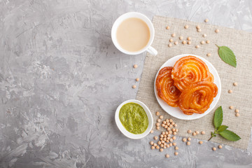 traditional indian candy jalebi in white plate with mint chutney on a gray concrete background. top view.