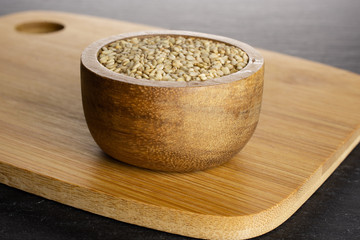 Lot of whole unpeeled sesame seeds in wooden bowl on chopping board on grey stone