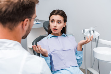 Obraz premium selective focus of attractive woman showing shrug gesture near dentist in clinic