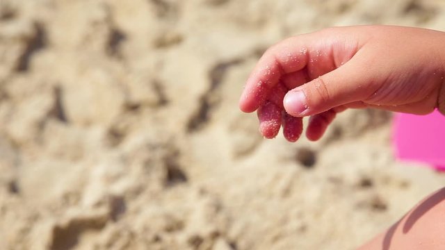 The child plays with sand on summer beach.