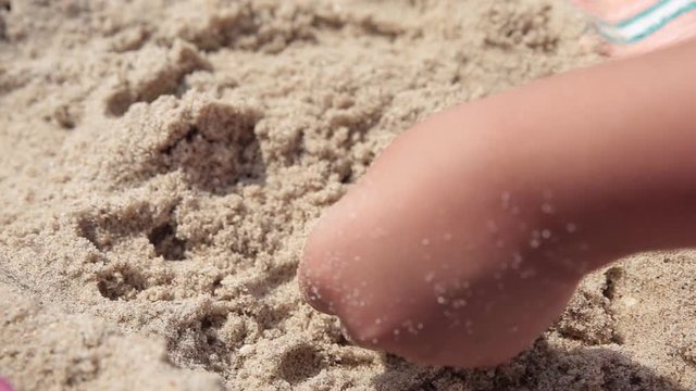 The child plays with sand on summer beach.