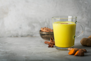 Golden turmeric milk on the gray background with ingredients