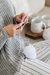 girl in a warm gray sweater knits sitting on a sofa in a cozy interior hygge