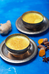 Golden turmeric milk on the blue background with ingredients