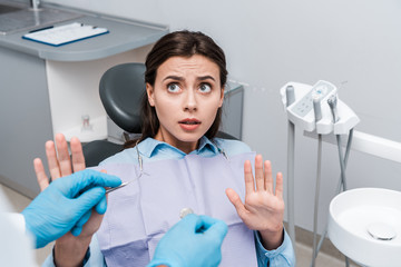 selective focus of scared woman looking at dentist with dental instruments