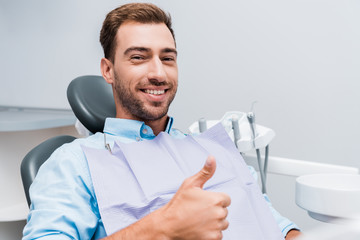 happy bearded man smiling while showing thumb up in dental clinic