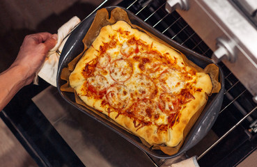 hot pizza taken out of the oven, top view, man holding a baking dish