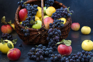 Autumn still life with apples and grapes located on a dark background, Apples and grapes in a basket