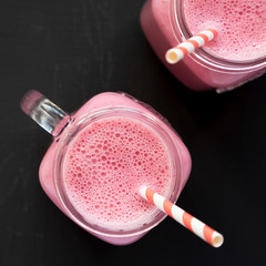 Raspberry smoothie in glass jars on a black background, top view. Overhead, from above, flat lay.