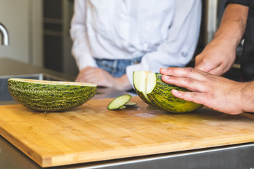 Young Male Chef Cutting Melon on Cutting Board.