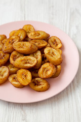 Homemade fried plantains on a pink plate on a white wooden surface, side view. Close-up.