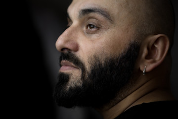 Close-up portrait of bearded bald man with earring. Black, dark background