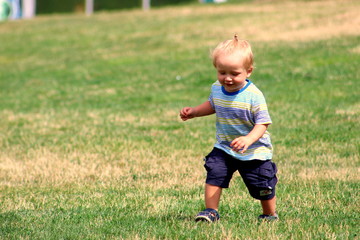 Fototapeta premium Cute toddler boy blond European appearance close-up in gray clothes in the park smiling selective focus.