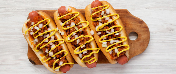 Homemade detroit style chili dog on a rustic wooden board on a white wooden surface, overhead view....
