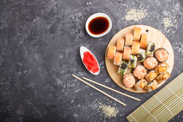 Mixed japanese maki sushi rolls set with chopsticks, ginger, soy sauce,rice on black concrete background, top view.