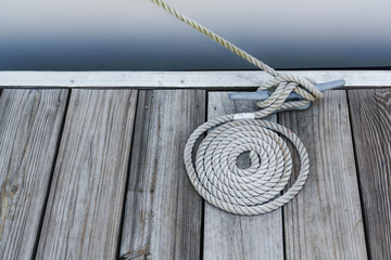 coil of rope on weathered wood deck tied onto a cleat