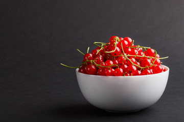 Fresh red currant in white bowl on black background. side view.