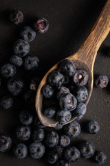 Blueberry berries in a wooden shabby spoon on a black table. Country style. Top view.