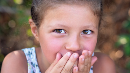 Authentic shot of cute little shy girl is smiling in camera on a green background a sunny day.