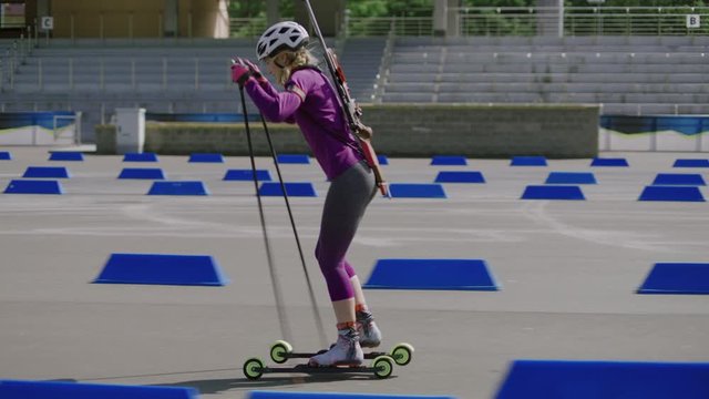 TRACKING SIDE VIEW Caucasian female professional biathlete roller skiing on a stadium during mid-season practice in summer. ARRI Alexa Mini with Cooke S4 prime lenses RAW graded footage