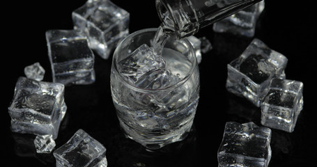 Pouring up shot of vodka from a bottle into glass. Black background