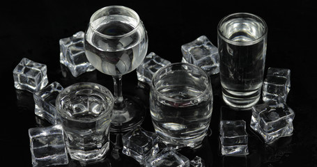 Shots of vodka with ice cubes against black background
