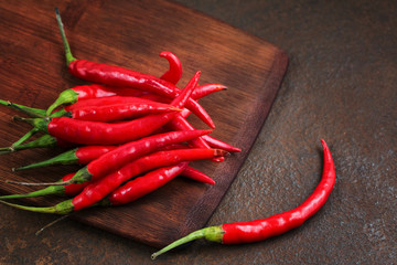 Pods of hot red pepper on a wooden board on a rusty metal surface.