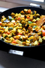 Stir frying seasonal vegetables in a wok. Chopped zucchini, tomato, eggplant and carrot, seasoned with turmeric. Selective focus.