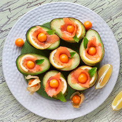 Avocado boats with smoked salmon, lemon, physalis and mint leaf, top view