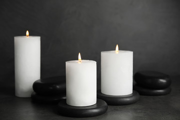 Fototapeta na wymiar Burning candles and black spa stones on grey table