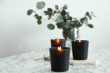 Burning candles and green branches with fairy lights on marble table