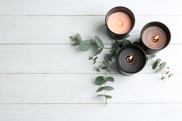 Burning candles and green branches on white wooden table, flat lay. Space for text